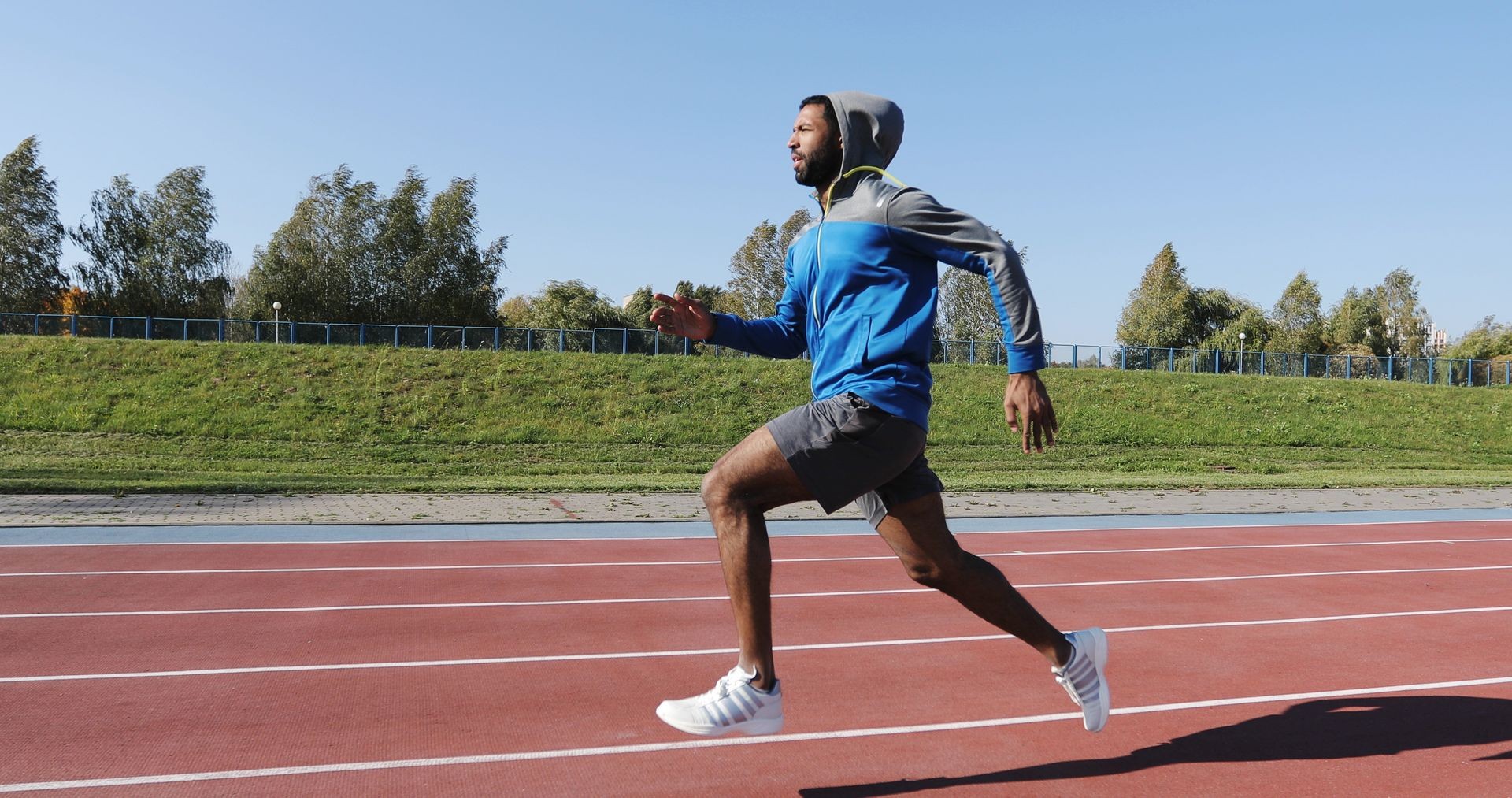 Young African male athlete sprinting alone down a running track on a sunny day. Black man training outdoors.